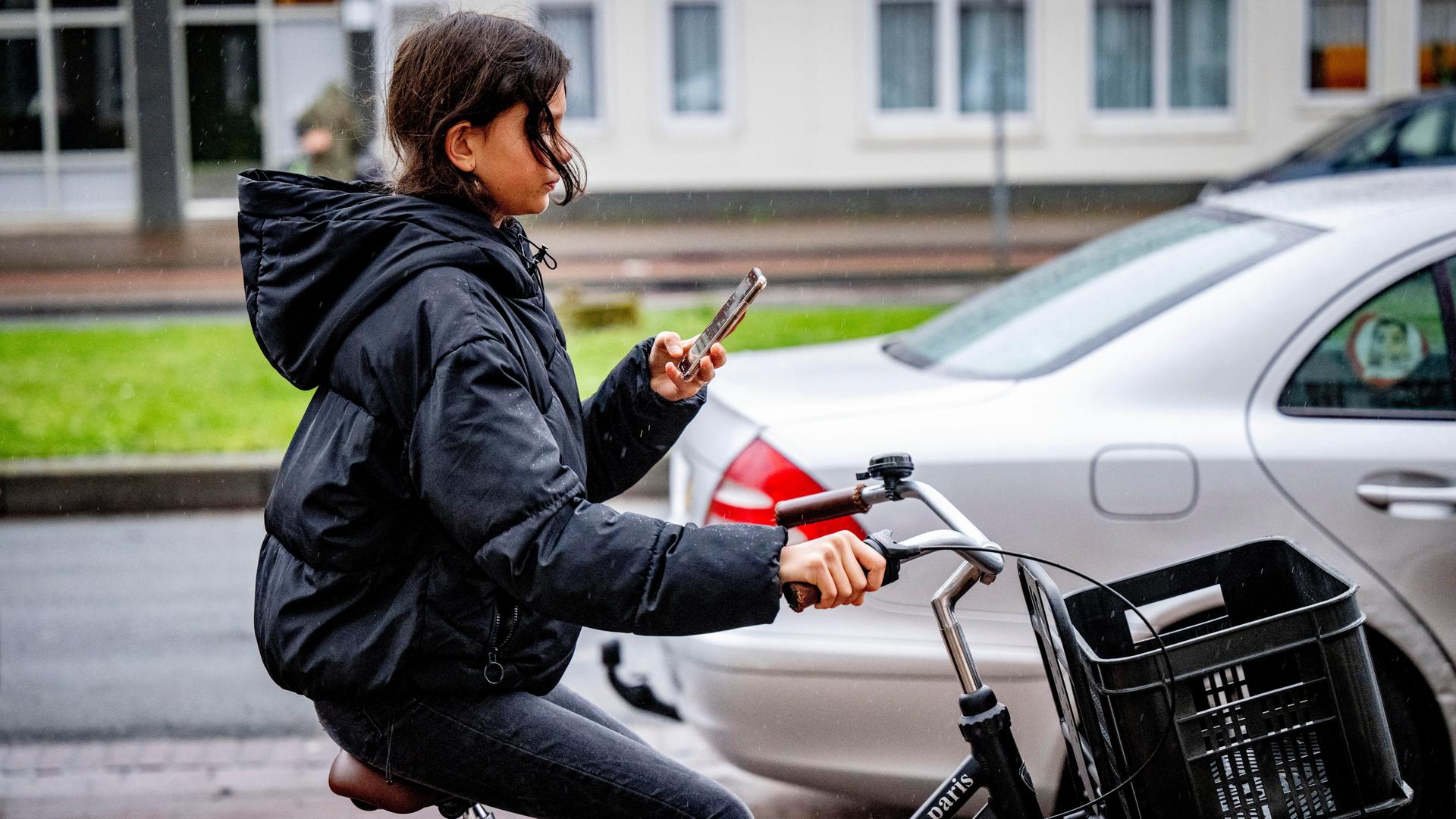 Eine junge Frau schaut auf ihr Mobiltelefon während sie Fahrrad fährt Eine junge Frau schaut auf ihr Mobiltelefon während sie Fahrrad fährt