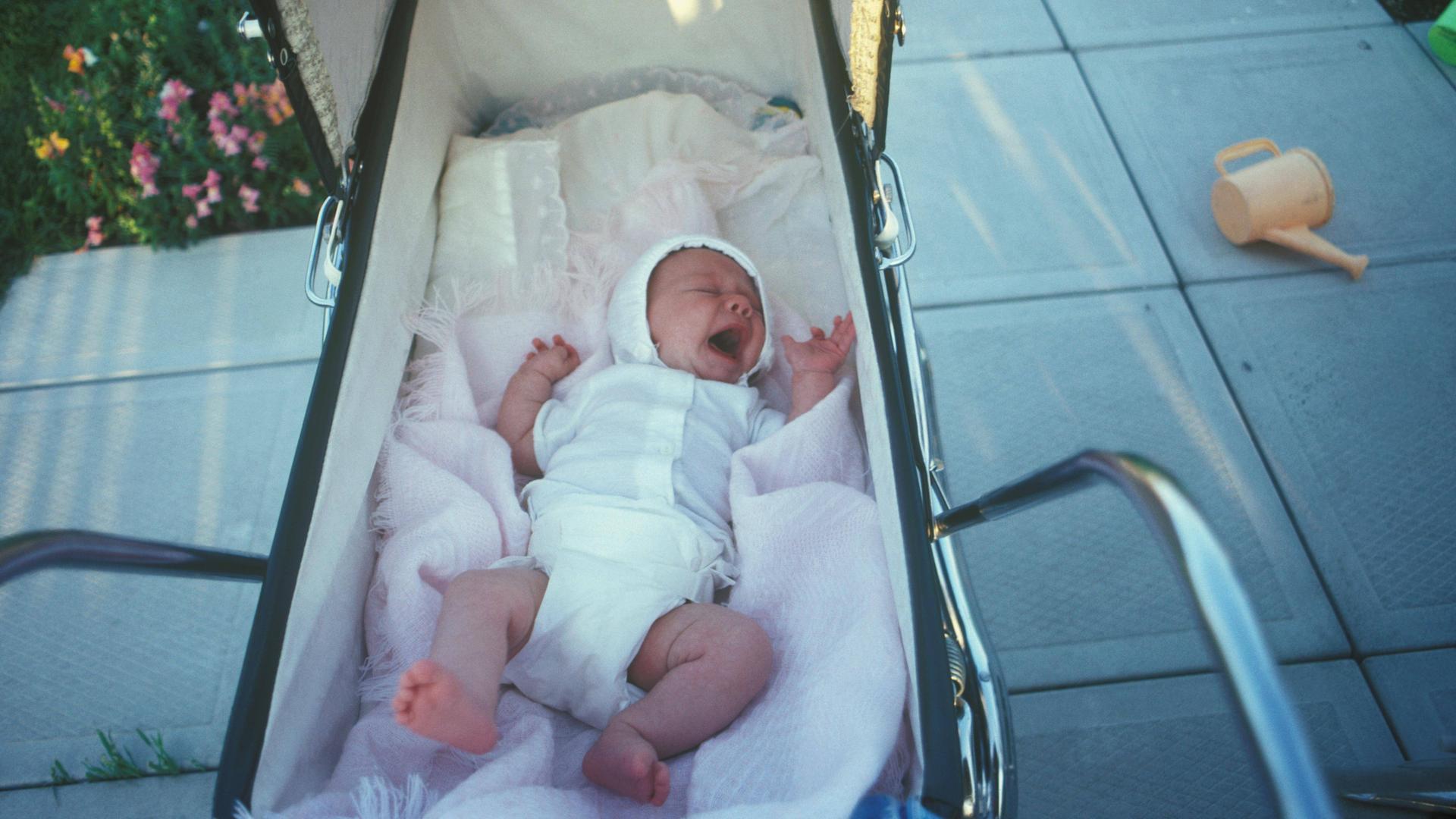 Ein neugeborenes Baby weint im einem Kinderwagen. Ein Foto aus einem privaten Familienalbum.