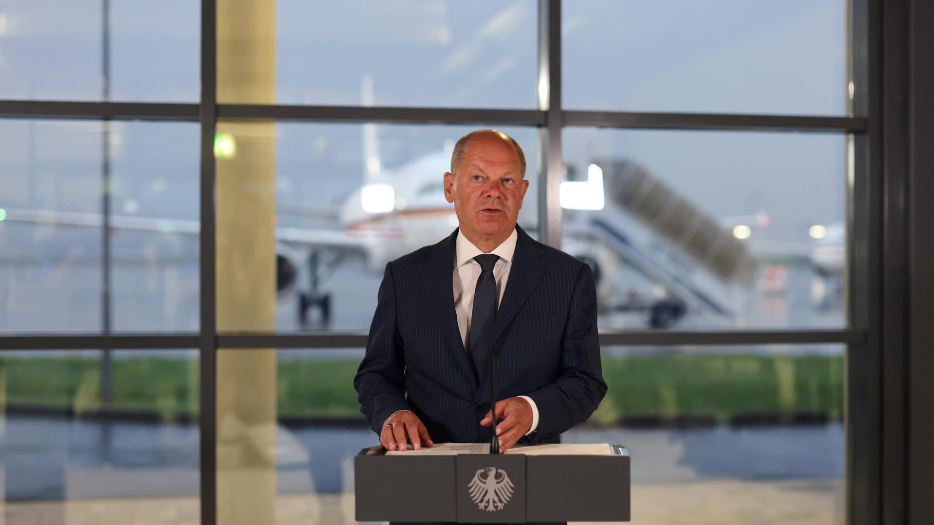 Bundeskanzler Olaf Scholz spricht bei einer Pressekonferenz auf einem Flughafen. 