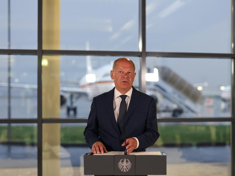 Bundeskanzler Olaf Scholz spricht bei einer Pressekonferenz auf einem Flughafen. 