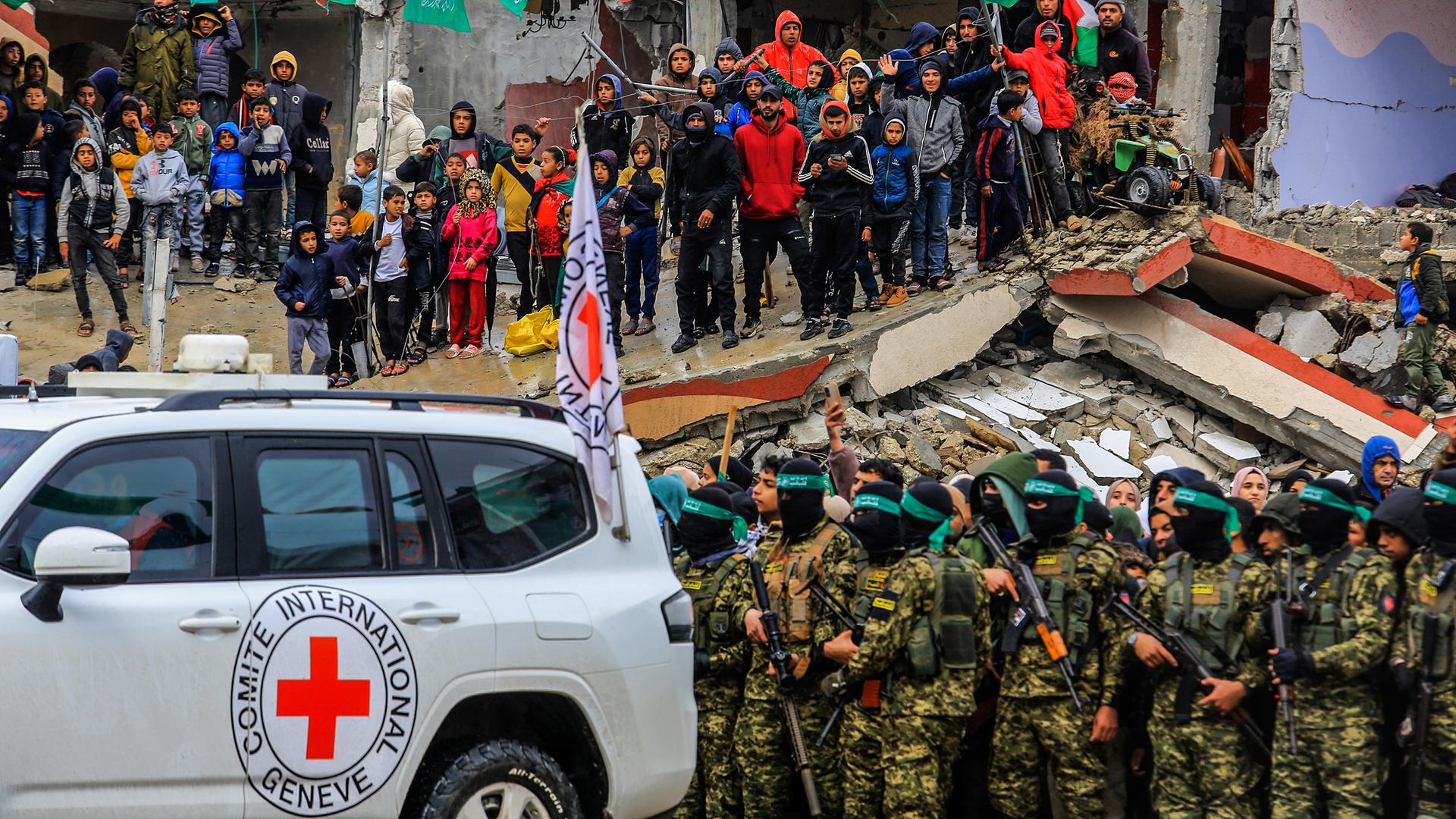 Palästinenser schauen zu, wie zwei israelische Geiseln von vermummten und bewaffneten Mitgliedern der Terrororganisation Hamas in Rafah im südlichen Gazastreifen an das Internationale Rote Kreuz (IKRK) übergeben werden.