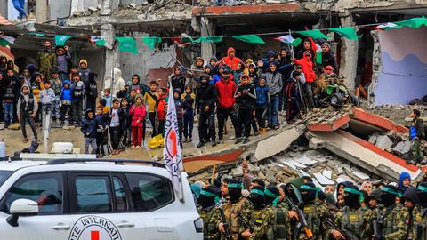 Palästinenser schauen zu, wie zwei israelische Geiseln von vermummten und bewaffneten Mitgliedern der Terrororganisation Hamas in Rafah im südlichen Gazastreifen an das Internationale Rote Kreuz (IKRK) übergeben werden.