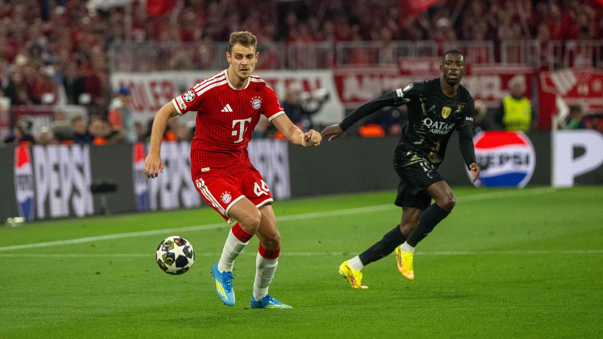 Zwei Männer spielen Fußball auf dem Rasen, der rechte trägt ein rotes, der linke ein schwarzes Trikot.