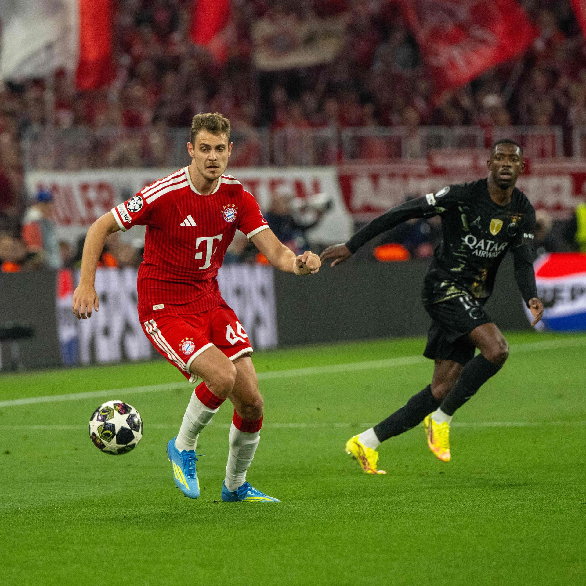 Zwei Männer spielen Fußball auf dem Rasen, der rechte trägt ein rotes, der linke ein schwarzes Trikot.