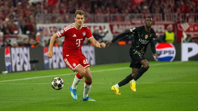 Zwei Männer spielen Fußball auf dem Rasen, der rechte trägt ein rotes, der linke ein schwarzes Trikot.