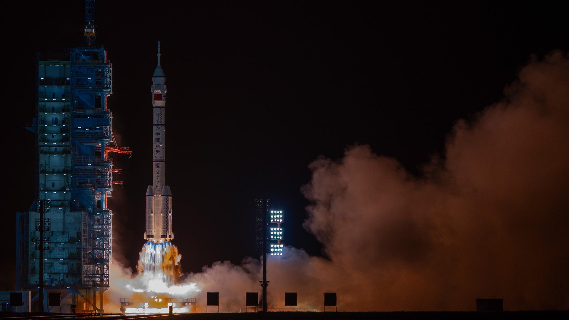 Das Bild zeigt den Start einer Trägerrakete bei Nacht. Unter den Triebwerken sind ein Feuerschweif und große Rauchschwaden zu sehen.