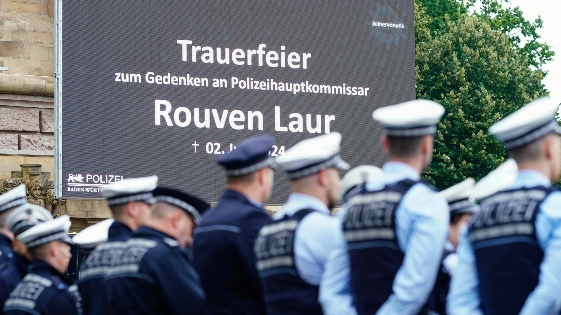 Polizisten stehen bei einer öffentliche Trauerfeier für den getöteten Polizisten Rouven Laur vor einer Leinwand. 