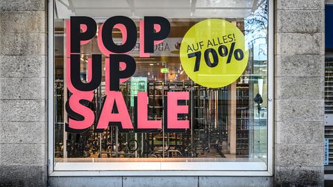 Das Schaufenster eines leerstehenden Kaufhauses ist mit großen Sale-Ankündigungen beklebt. Innen sind leere Kleiderständer zu sehen.