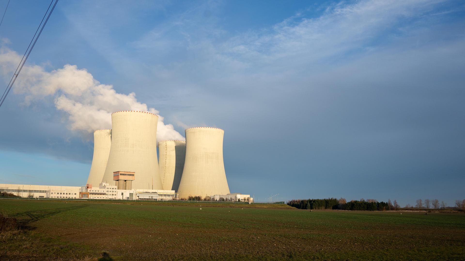 Im Hintergrund stehen Kühltürme einer Atomkraftanlage, aus denen Dampf aufsteigt vor einem blauen Himmel. Im Hintergrund stehen Kühltürme einer Atomkraftanlage, aus denen Dampf aufsteigt vor einem blauen Himmel.