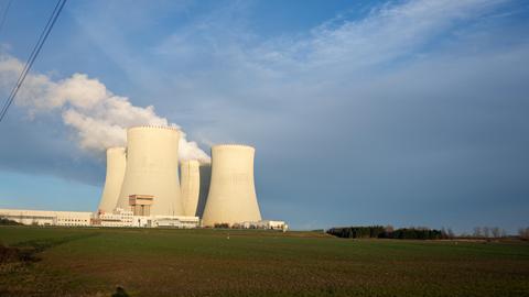 Im Hintergrund stehen Kühltürme einer Atomkraftanlage, aus denen Dampf aufsteigt vor einem blauen Himmel.