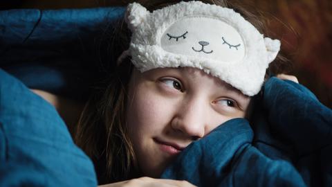 Junge schläfrige Frau, die unter Schlaflosigkeit leidet und eine Schlafmaske trägt.