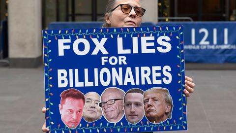 Eine Demonstrantin hält ein Schild mit der Aufschrift „FOX LIES FOR BILLIONAIRES” (FOX LÜGT FÜR MILLIARDÄRE) mit Bildern von Musk, Bezos, Murdoch, Zuckerberg und Trump vor dem Fox News Channel in New York City, USA, November 2025. Eine Demonstrantin hält ein Schild mit der Aufschrift „FOX LIES FOR BILLIONAIRES” (FOX LÜGT FÜR MILLIARDÄRE) mit Bildern von Musk, Bezos, Murdoch, Zuckerberg und Trump vor dem Fox News Channel in New York City, USA, November 2025.