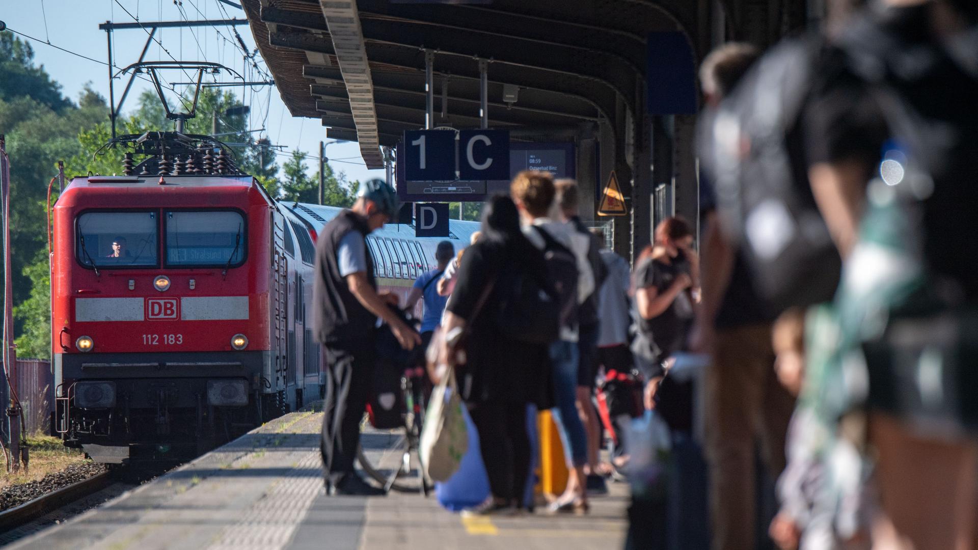 Ein Regionalzug fährt in einen Bahnhof ein. Am Gleis warten Menschen. Ein Regionalzug fährt in einen Bahnhof ein. Am Gleis warten Menschen.