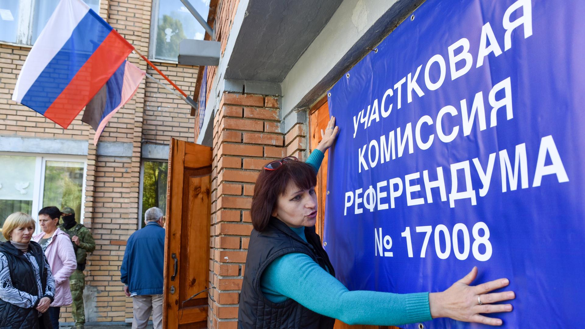 Eine Frau hängt ein Banner für das Scheinreferendum in Donezk auf. 