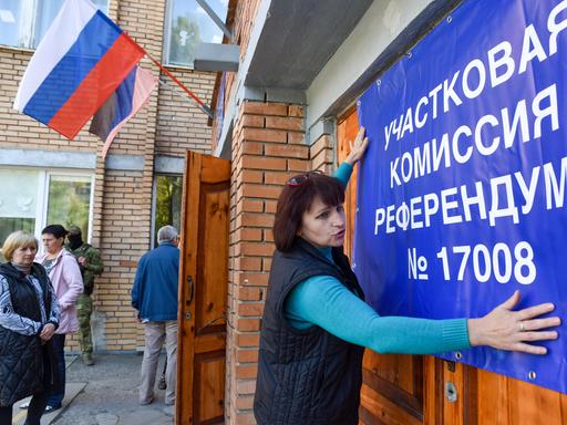 Eine Frau hängt ein Banner für das Scheinreferendum in Donezk auf. 