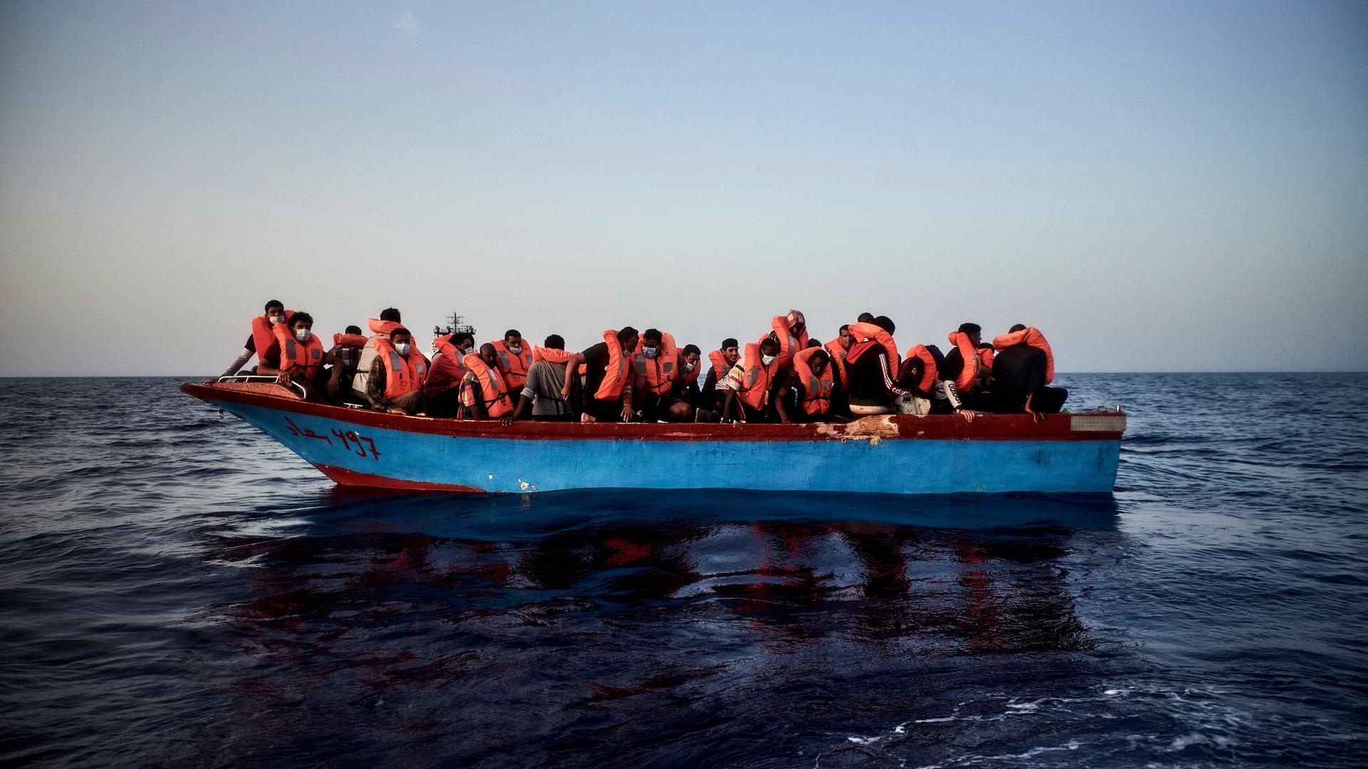 Flüchtlinge mit Rettungswesten auf einem überfüllten Boot im Meer.