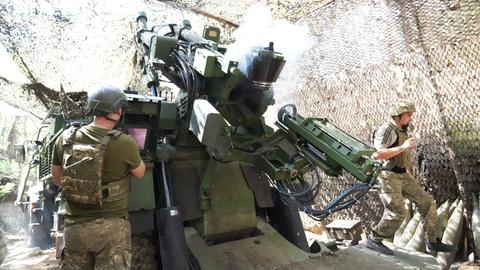 Soldaten feuern ein Artilleriegeschütz in einer getarnten Deckung ab. 