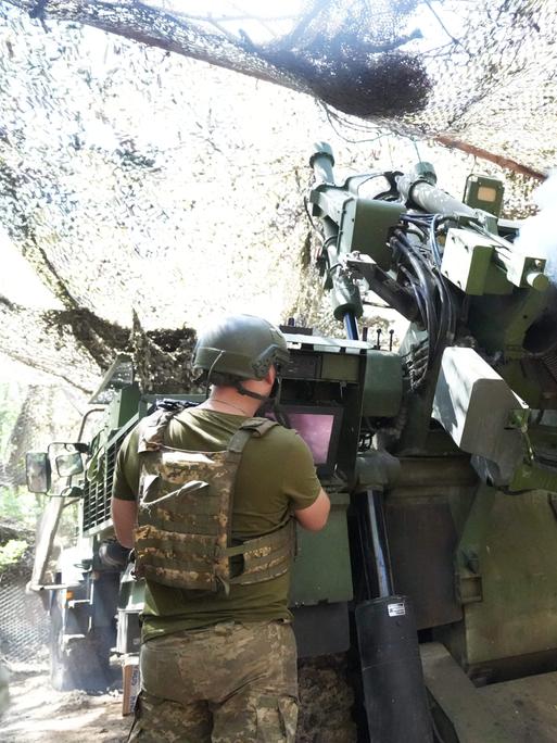 Soldaten feuern ein Artilleriegeschütz in einer getarnten Deckung ab. 