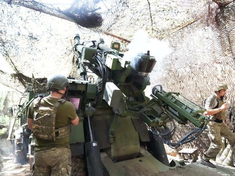 Soldaten feuern ein Artilleriegeschütz in einer getarnten Deckung ab. 