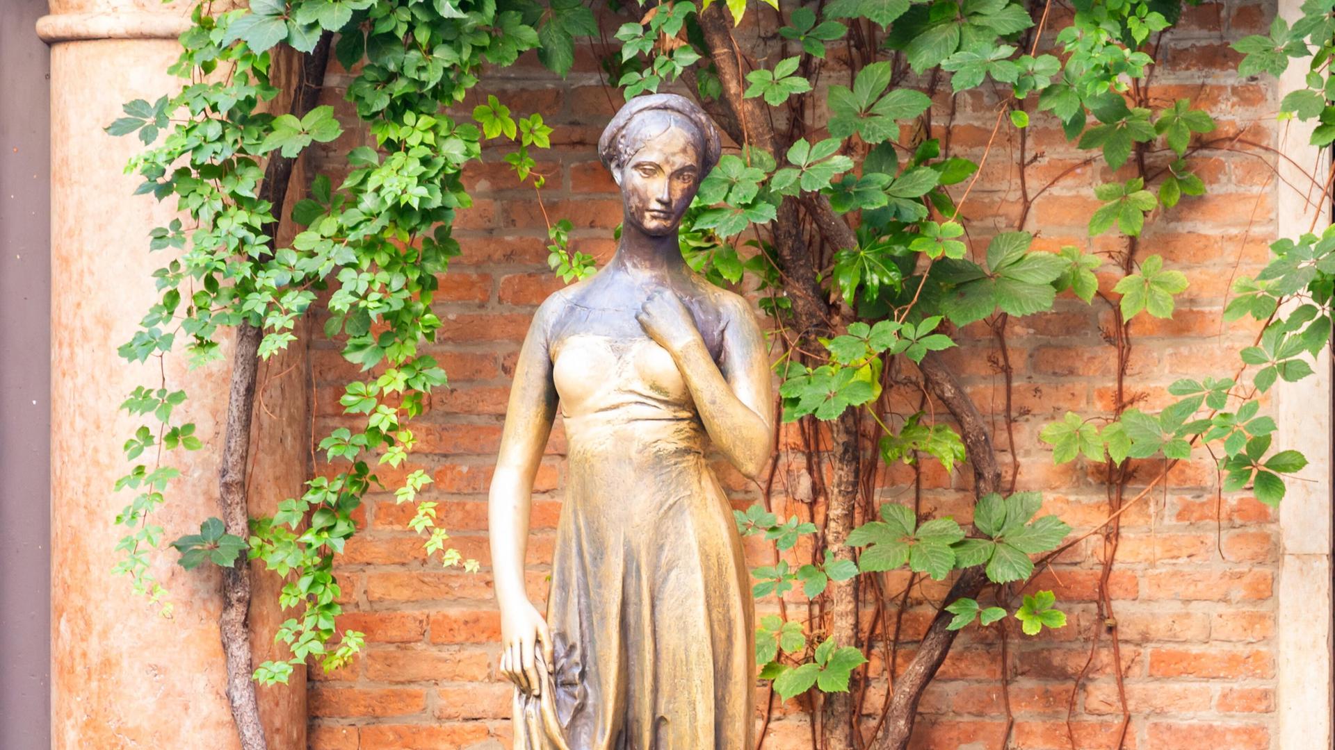 Die Julia-Statue steht vor einem weinumragten Mauerwerk in Verona