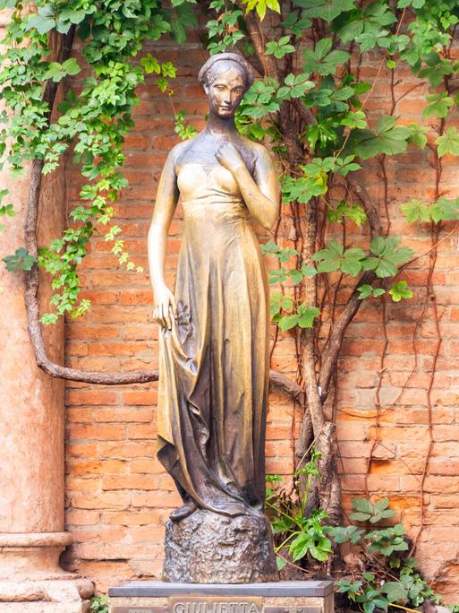 Die Julia-Statue steht vor einem weinumragten Mauerwerk in Verona