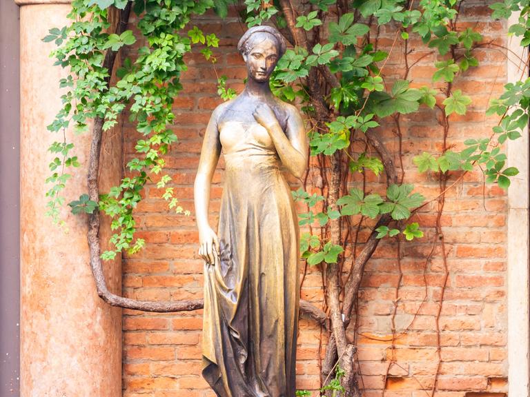 Die Julia-Statue steht vor einem weinumragten Mauerwerk in Verona