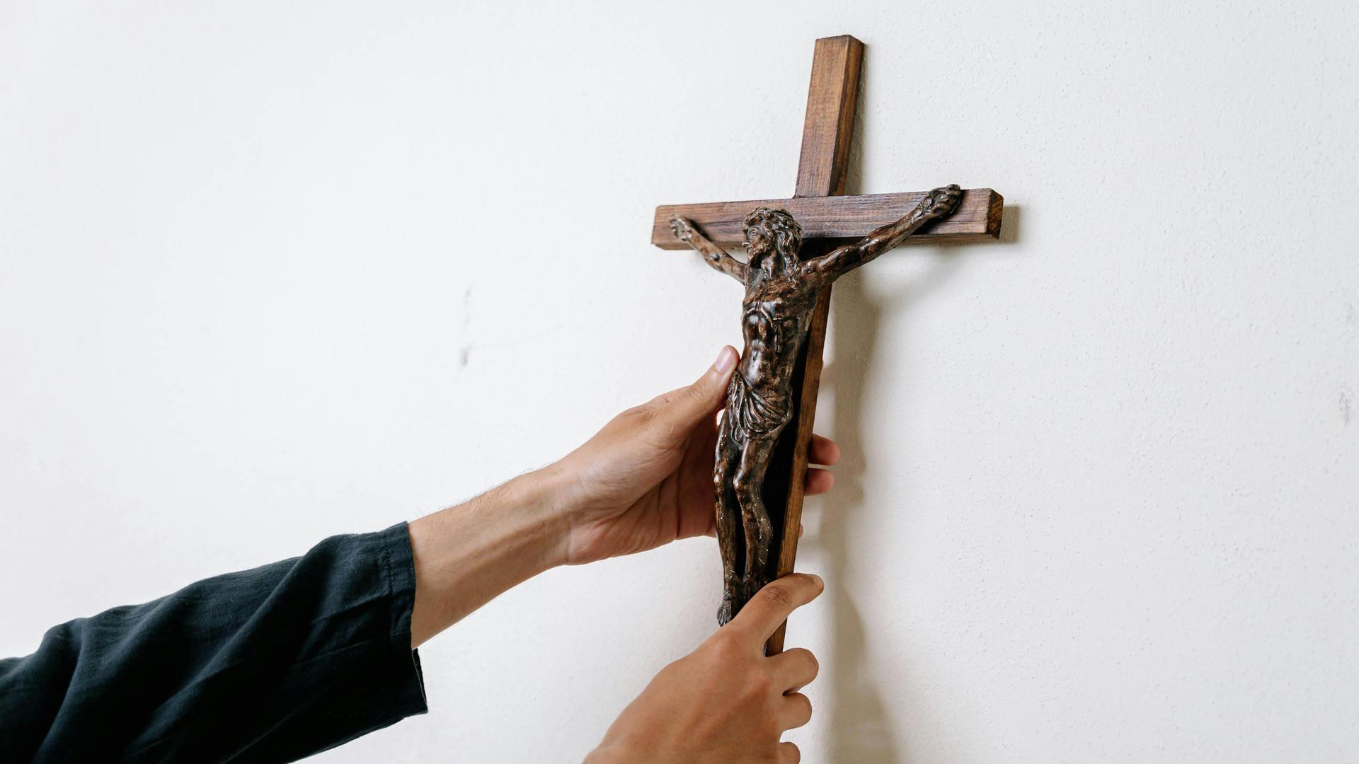 Ein Mann hängt ein Kruzifix an eine Wand. Ein Mann hängt ein Kruzifix an eine Wand.