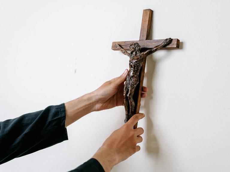 Ein Mann hängt ein Kruzifix an eine Wand.