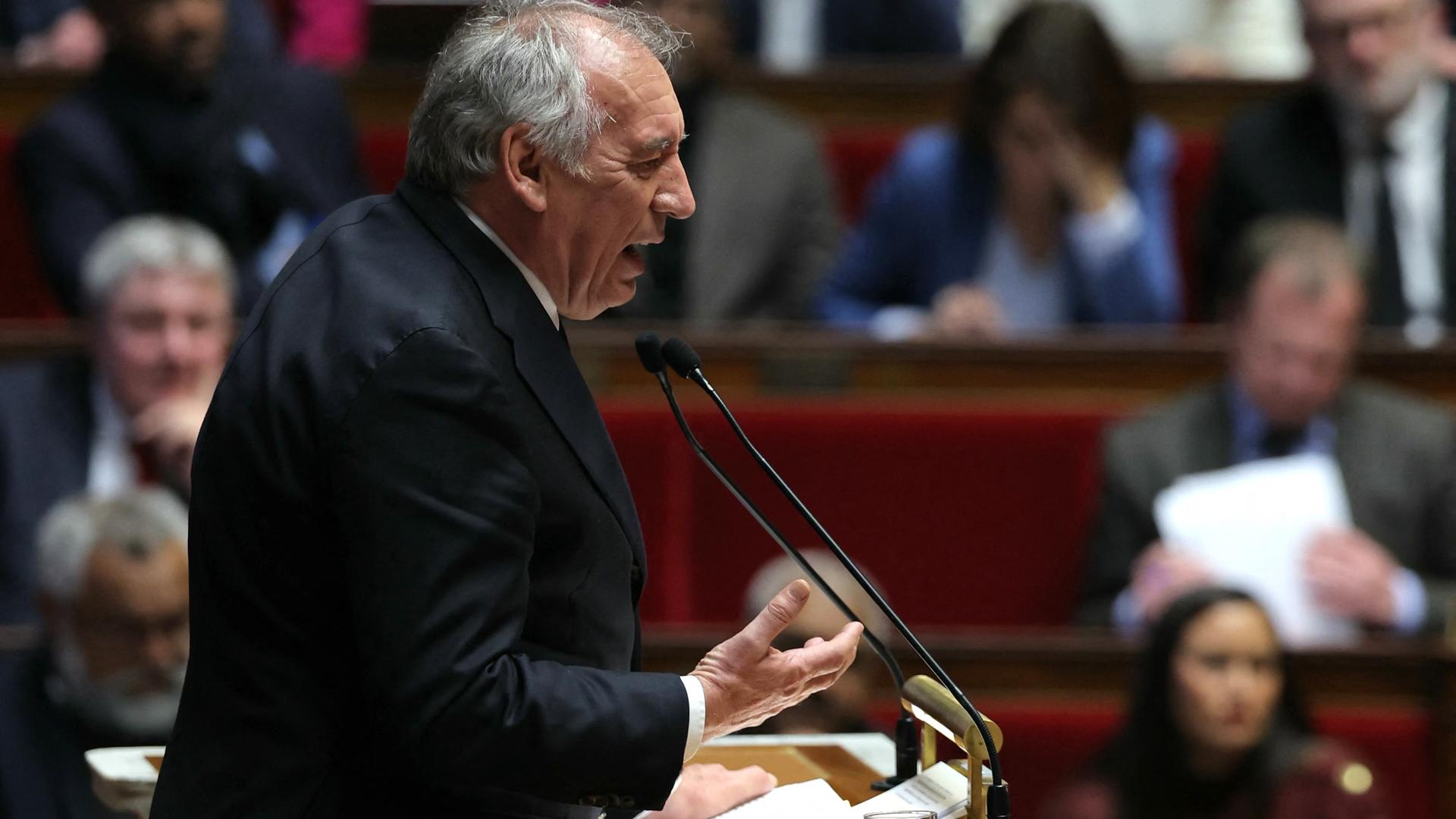 Der französische Premierminister Bayrou steht in der Nationalversammlung am Rednerpult und gestikuliert mit seiner rechten Hand. 