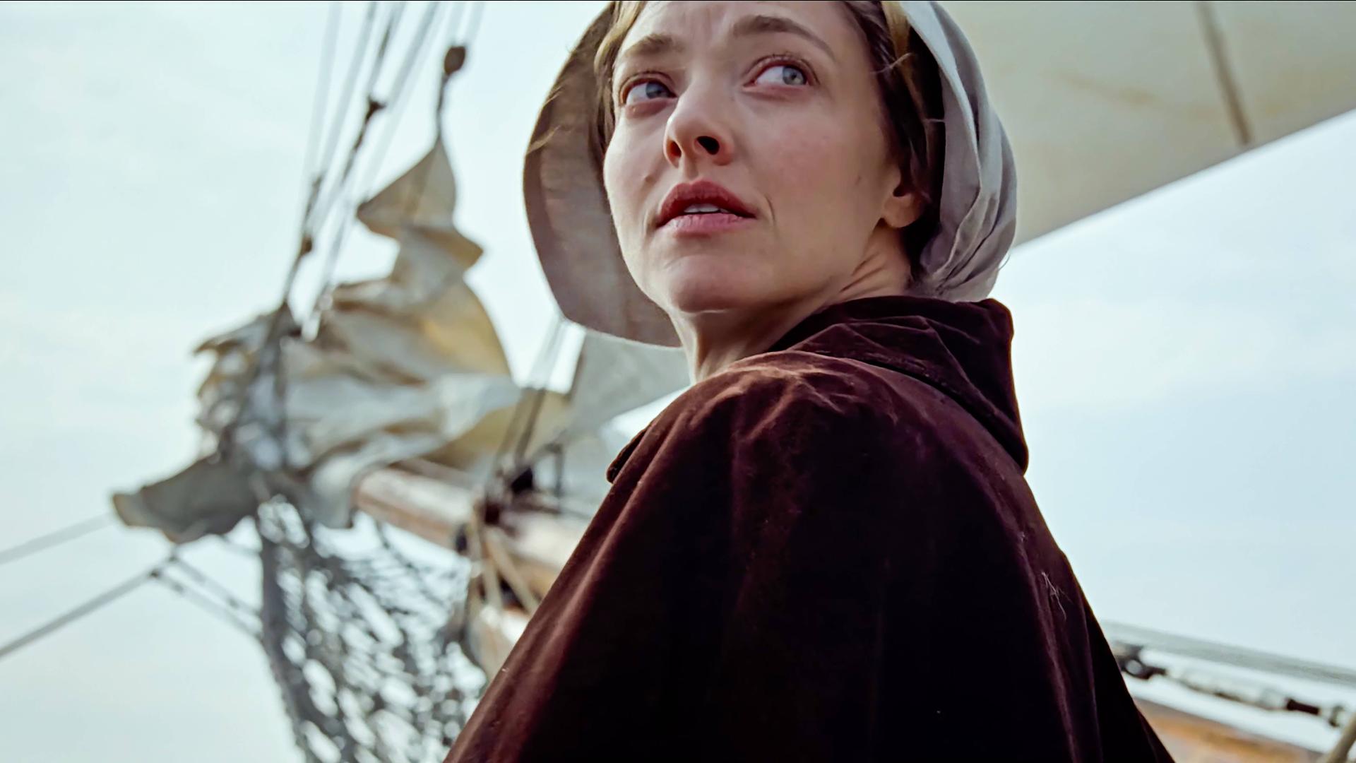 Die Hauptdarstellerin Amanda Seyfried in ihrer Rolle als Ann Lee dreht sich um. Im Hintergrund ist der Mast eines Bootes zu sehen, sie trägt eine traditionelle Kopfbedeckung. Die Hauptdarstellerin Amanda Seyfried in ihrer Rolle als Ann Lee dreht sich um. Im Hintergrund ist der Mast eines Bootes zu sehen, sie trägt eine traditionelle Kopfbedeckung.