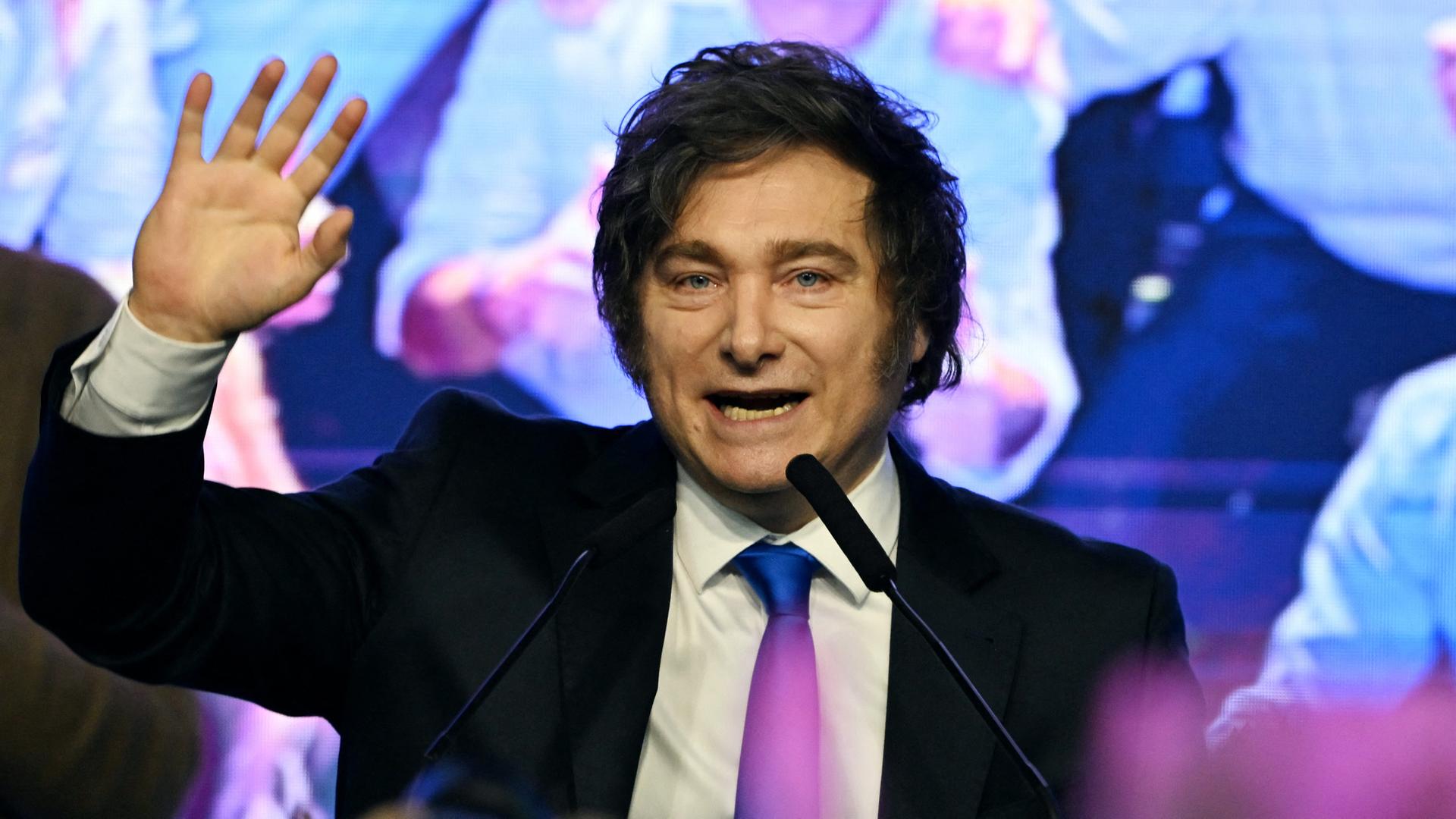 Argentiniens Präsident Javier Milei steht vor einem Mikrofon und winkt ins Publikum.