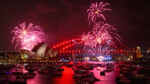 Silvesterfeiern im australischen Sydney: Zu sehen ist der Hafen mit der Harbour Bridge und der Oper, vorne im Bild sind viele Schiffe; am Himmel Feuerwerk