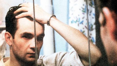 Ein Mann steht vor einem Spiegel und schaut sich ins Gesicht