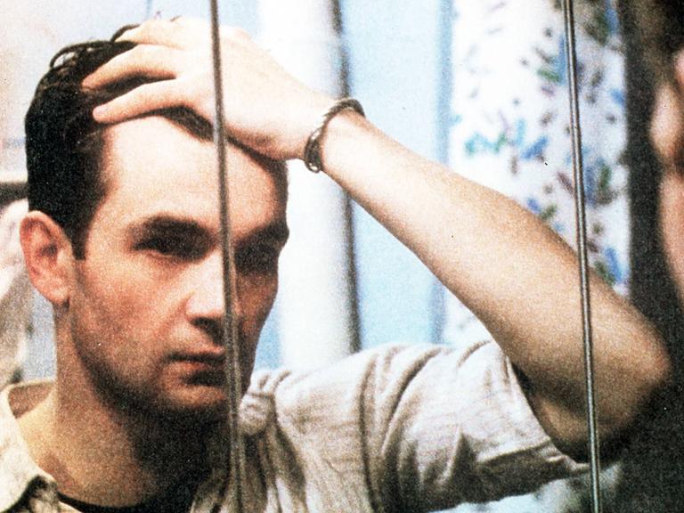 Ein Mann steht vor einem Spiegel und schaut sich ins Gesicht