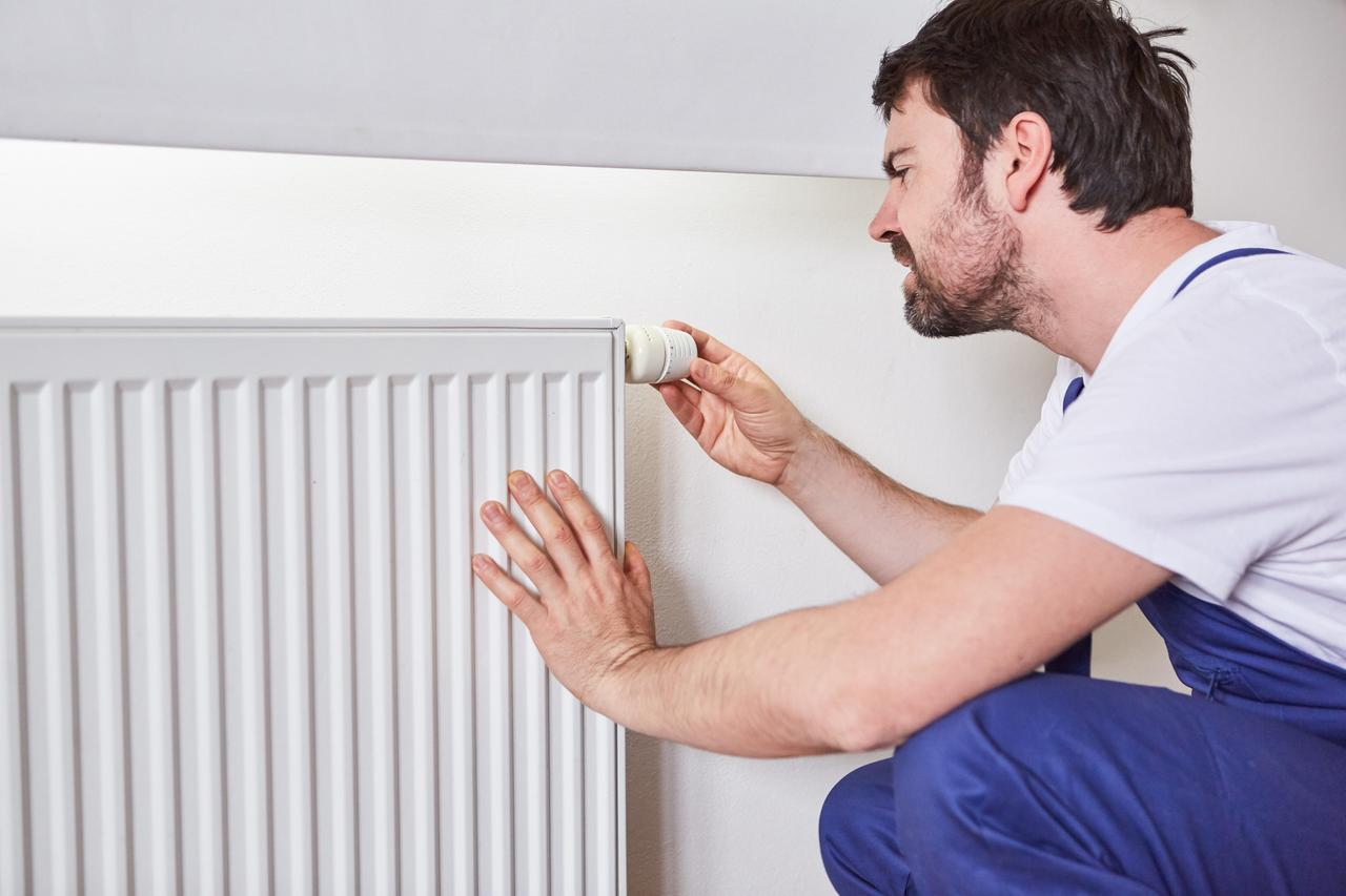 Ein Installateur justiert den Thermostat an einem Heizkörper.