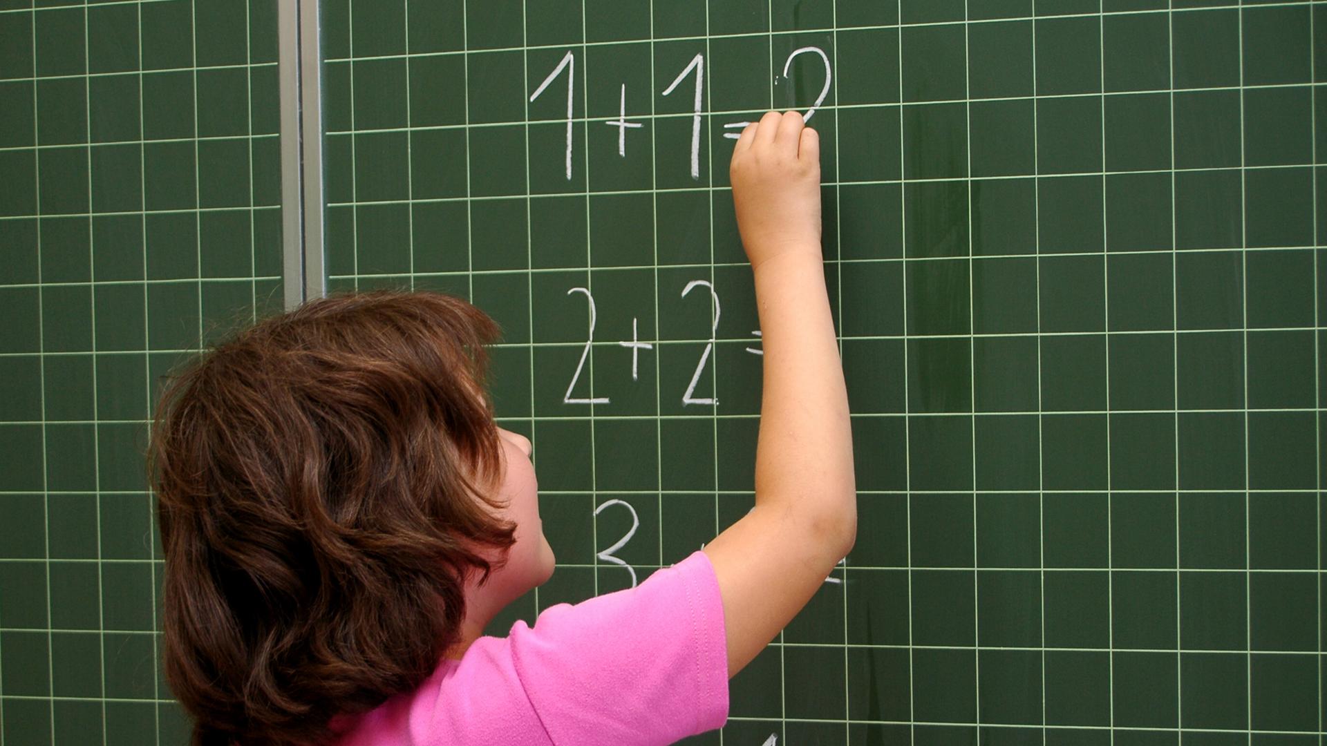 Ein Kind schreibt Zahlen an die Schul-Tafel.