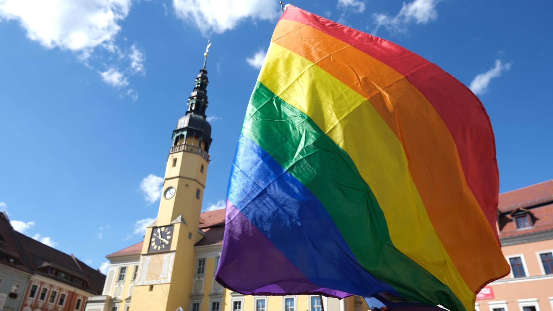 Eine Regenbogenflagge weht in der Luft bei blauem Himmel auf einem Platz in Bautzen beim CSD 2024. 