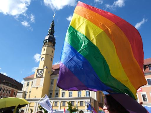 Eine Regenbogenflagge weht in der Luft bei blauem Himmel auf einem Platz in Bautzen beim CSD 2024. 