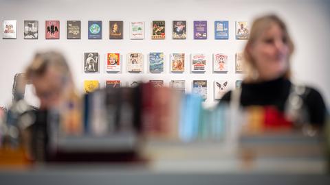Eine weiße Wand mit vielen Büchern ist im Fokus, davor stehen zwei Personen im Vordergrund verschwommen