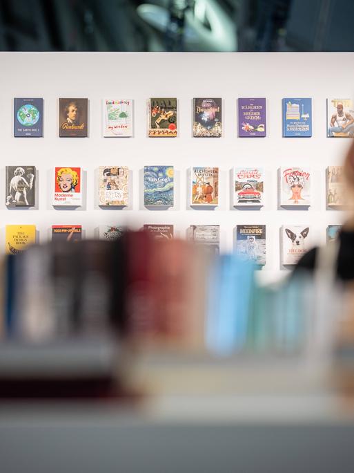 Eine weiße Wand mit vielen Büchern ist im Fokus, davor stehen zwei Personen im Vordergrund verschwommen