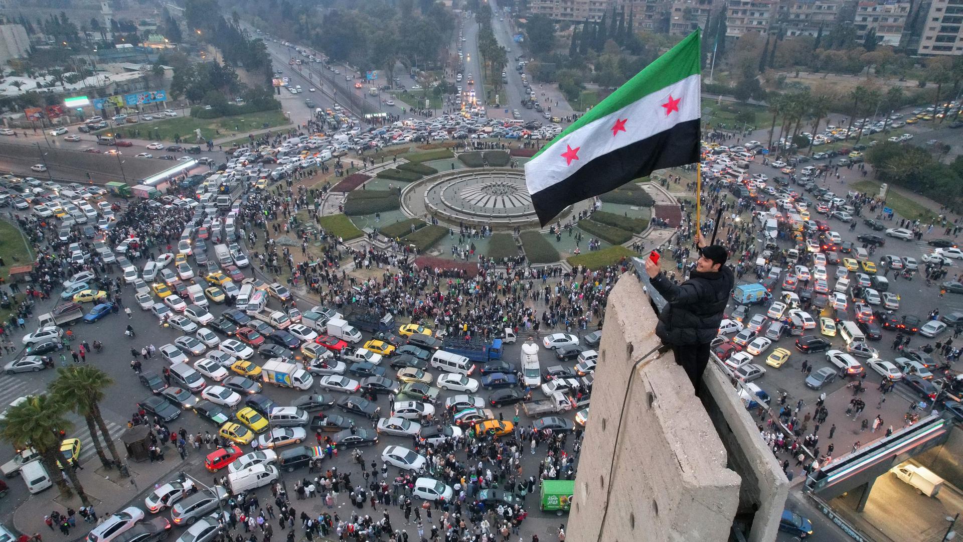 Ein Mann schwenkt die syrische Oppositionsflagge auf einem Denkmal auf dem zentralen Umayyad-Platz in Damaskus.