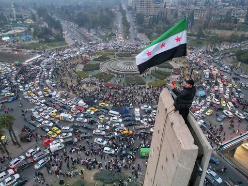 Ein Mann schwenkt die syrische Oppositionsflagge auf einem Denkmal auf dem zentralen Umayyad-Platz in Damaskus.