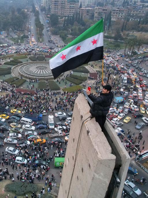 Ein Mann schwenkt die syrische Oppositionsflagge auf einem Denkmal auf dem zentralen Umayyad-Platz in Damaskus.