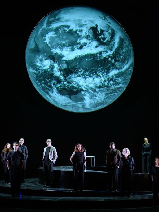 Szenenfoto aus der Produktion "Wir sind das Volk" am Deutschen Nationaltheater Weimar: Schauspielende auf einer dunklen Bühne blicken Richtung Publikum, hinter ihnen eine Projektion der Erdkugel. Szenenfoto aus der Produktion "Wir sind das Volk" am Deutschen Nationaltheater Weimar: Schauspielende auf einer dunklen Bühne blicken Richtung Publikum, hinter ihnen eine Projektion der Erdkugel.