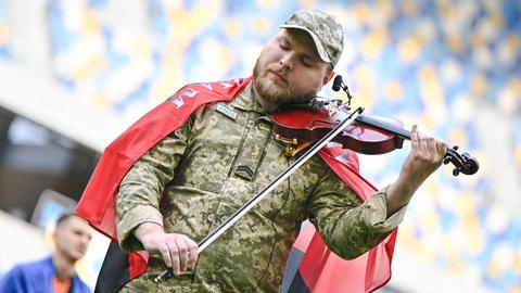 Moisei Bondarenko trägt eine Militär-Uniform und spielt mit geschlossenen Augen Geige in einem Stadion.