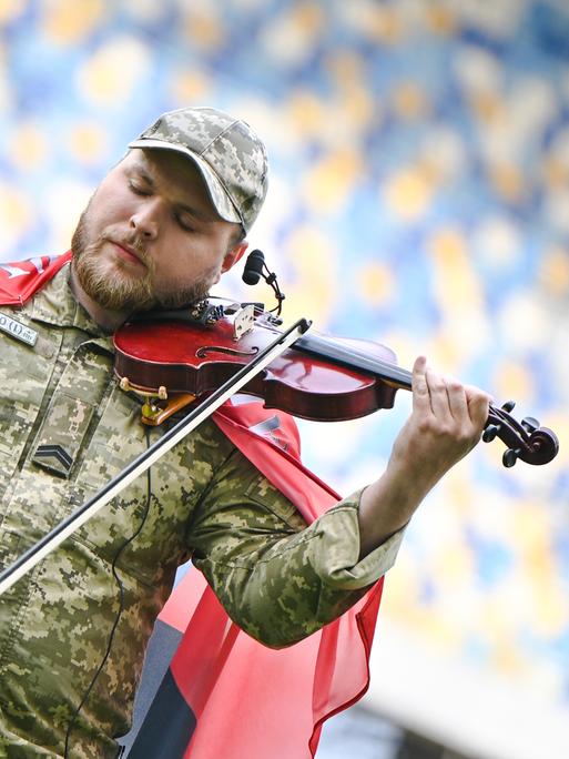 Moisei Bondarenko trägt eine Militär-Uniform und spielt mit geschlossenen Augen Geige in einem Stadion.