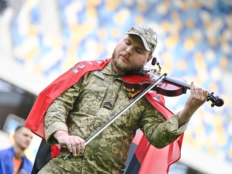 Moisei Bondarenko trägt eine Militär-Uniform und spielt mit geschlossenen Augen Geige in einem Stadion.