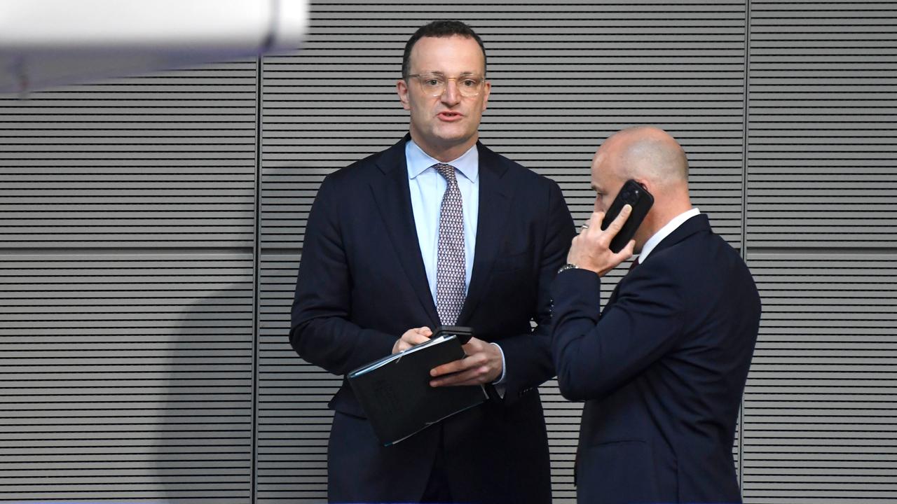 Jens Spahn steht bei der 19. Sitzung des 21. Deutschen Bundestages im Reichstagsgebäude und hält einen Ordner, daneben ein telefonierender Mann