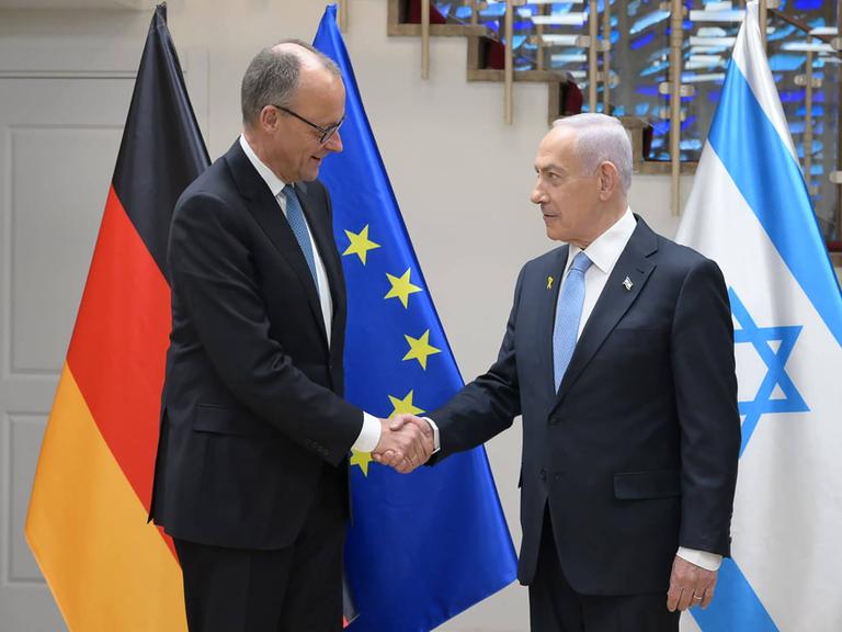 Friedrich Merz und Benjamin Nethanjahu stehen vor der deutschen und der israelischen Flagge und geben sich die Hand.