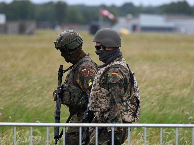 Soldaten der Bundeswehr gehen am Luftwaffenstützpunkt der Bundeswehr in Jagel durch hohes Gras.